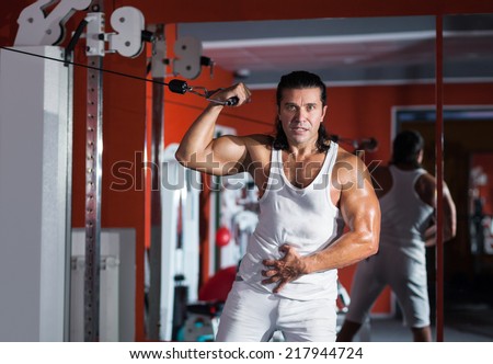 Sportive man works out with pull-down machine in the gym