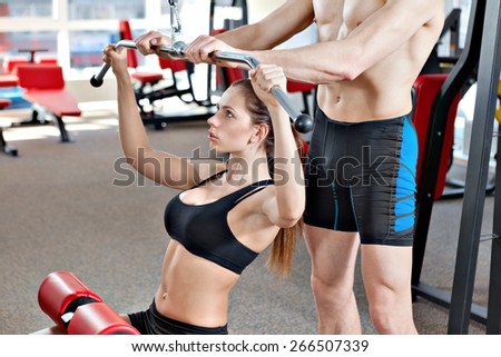 Woman at the health club with her personal trainer, learning the correct form on the pull down machine.