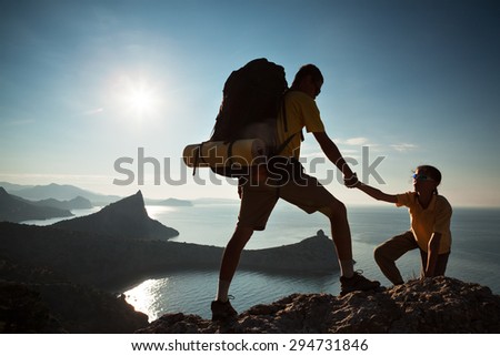 Backpacker helps to his friend to climb to rock