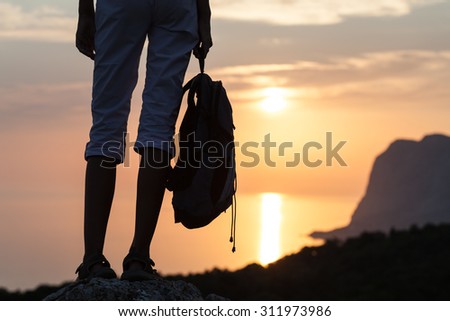 Young woman hiker legs and backpack on sunrise mountain rock