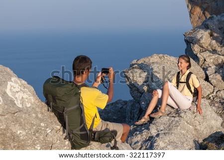 Hiking couple on the rock. Man takes photo of woman by compact camera.