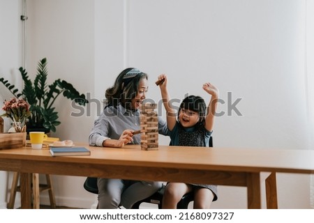 Similar – Image, Stock Photo Excited girl playing jenga game with her mom in play room. Girl removing one block from stack and placing it on top of tower. Game of skill and fun. Family time