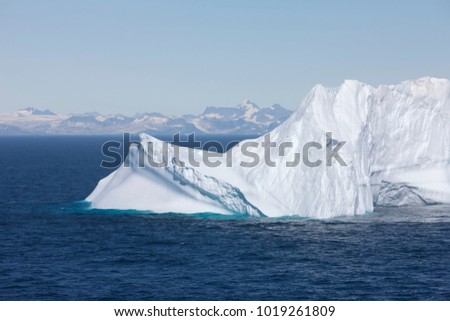 white Iceberg wall. Deep blue ocean surface with floating iceberg and greenland coast background