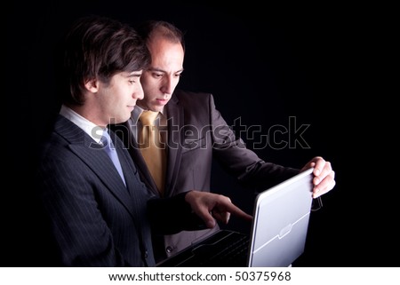 Two businessmen working together on a laptop, isolated on black background
