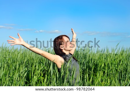 young woman with hands raised up in the wheat field over blue sky in summer