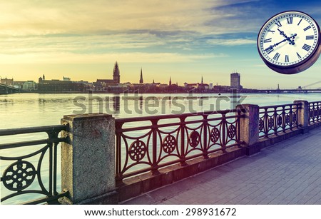 View on the Daugava river and old Riga city, Latvia. Clock dial can symbolize the time passing during vacation. Image slightly toned for inspiration of retro style/