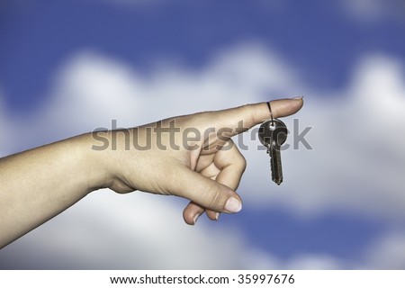 Hand having house keys on one finger with blue sky and clouds in background