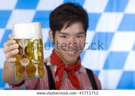 Asian man holding an Oktoberfest beer stein into camera and smiles happy. Focus on beer stein.   Isolated on white.