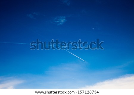 Vapor trail from an airplane in the blue sky, the moon and the plane