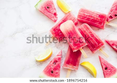 Homemade watermelon popsicles with ice against white marble background. Popsicles from frozen watermelon. Summer concept. Top view. Copy space.