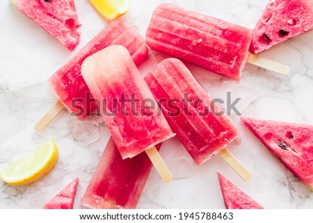 Homemade watermelon popsicles with ice against white marble background. Popsicles from frozen watermelon. Summer concept. Top view.