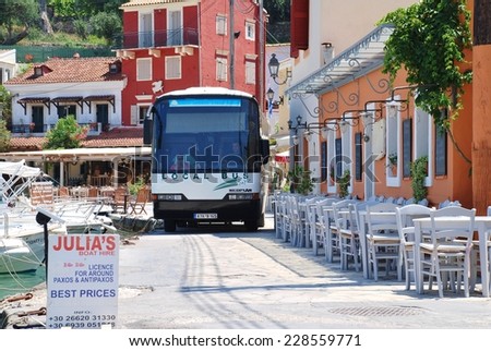 PAXOS, GREECE - JUNE 14, 2014: The local island bus negotiates the narrow seafront road at Loggos on the Greek island of Paxos. Taverna diners have to vacate their chairs to let the bus pass.