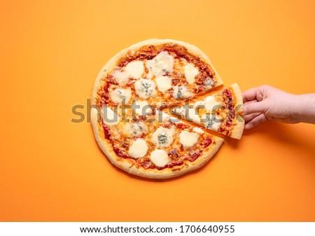 Quattro formaggi pizza and a woman hand taking one pizza slice, on an orange seamless background. Flat lay with 4 cheese pizza. Delicious Italian food.
