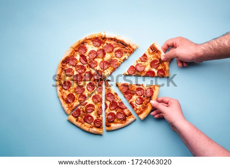 Man and woman hands grabbing pizza slices. Sliced pepperoni pizza on a blue background, above view. Top view with delicious pepperoni pizza.