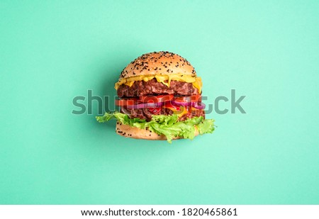 Homemade burger with double beef patties, cheese, and salad isolated on a green-mint background. Single hamburger side-view