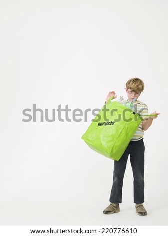 Young boy looking to camera while holding open a green bag with plastic items for recycling shot on a white background