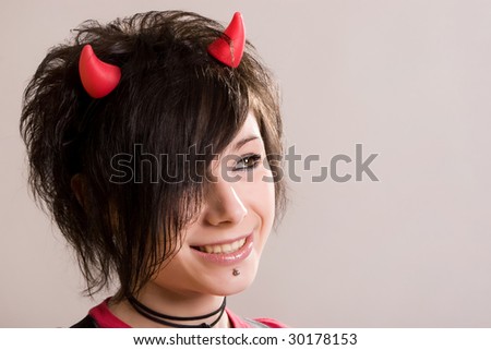 A young sexual  smiling girl in an image of a devil  in red and black with   horns on her head posing on a light background