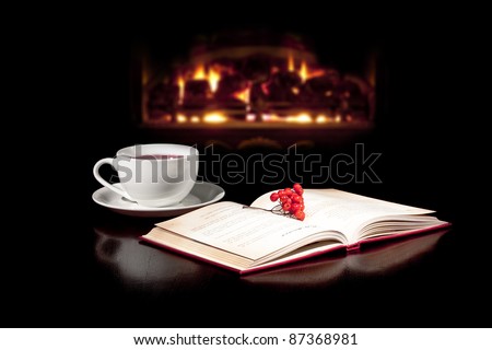 Cap of tea and book on the table top with fireplace in the background.