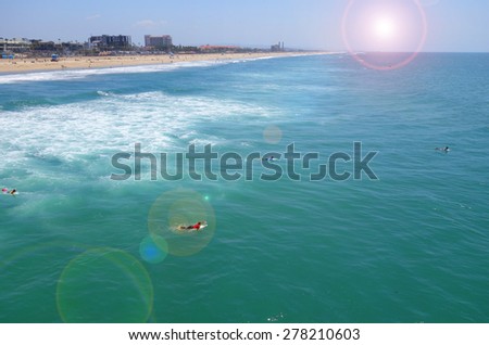 ocean and beach with bright sun flare and people swimming and surfing