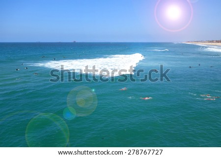 ocean and beach with surfers and swimmers and bright sun flare