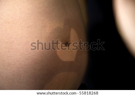 a heart mark or love heart being made by fathers hands casting a shadow over the mothers pregnant belly