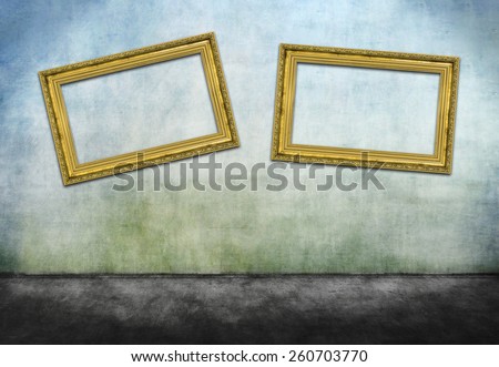 Two crooked golden frames on gray dirty wall