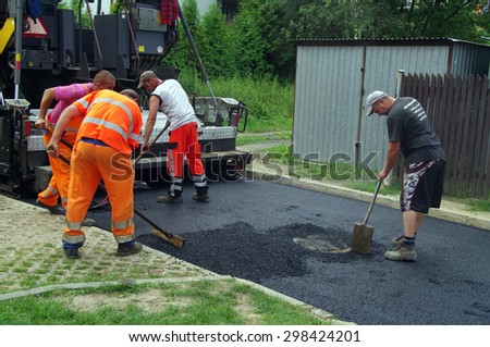 LUBLINIEC, POLAND - July 17, 2015 Brigade of workers repairs road with layer of raw asphalt material
