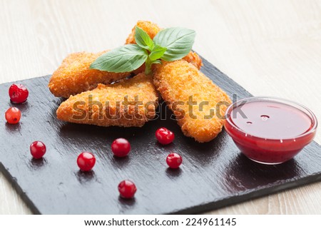 Appetizer fried cheese sticks served with basil, cranberries, and red berry sauce in bowl on black stone plate