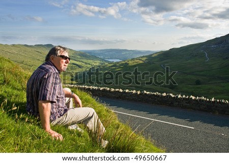Retired man resting near the road with beuatiful view in Lake District, England