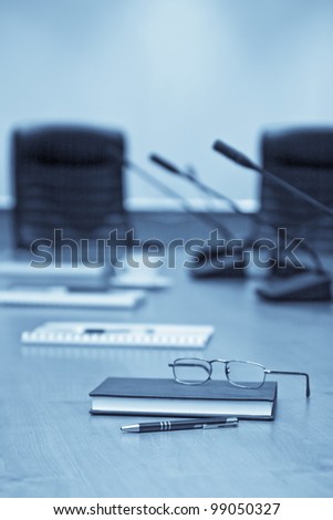 A close-up of a conference room showing a chairs, a table, a coffee cup,  and a note pad. Sharp focus on the pen.