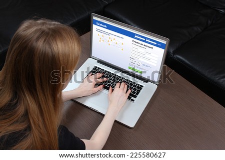 London, United Kingdom - September 24, 2014: Facebook homepage on computer screen teenage girl typing on laptop keyboard logging into famous social network Facebook home page and signing up