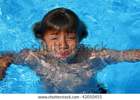 a 10-years old American - German boy having fun with diving and swimming in a swimming pool, photographed in the summer sun in that moment when just breaking through the water surface after diving