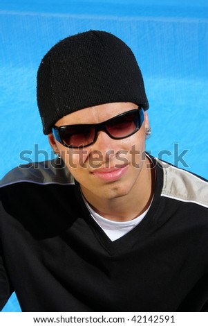 an arrogant looking teenager with sunglasses and a cap photographed in the summer sun sitting at a swimming pool