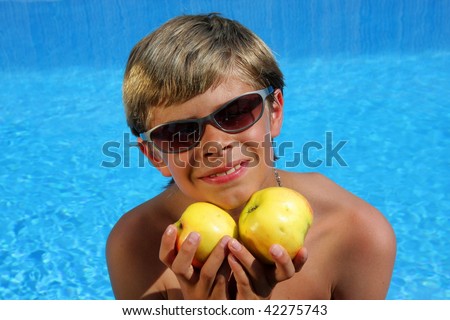 a 10-years old smiling American - German boy with sunglasses sitting at a swimming pool and presenting delicious apples in the summer sun
