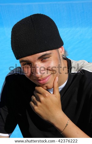 a happy smiling teenager with a cap photographed in the summer sun sitting at a swimming pool giving us a happy and satisfied smile