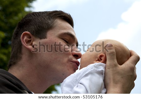 a happy and proud young father kissing his 7 weeks old crying daughter