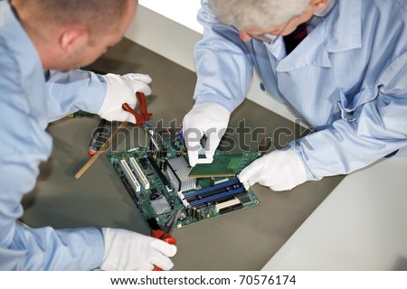 IT engineers working on a motherboard and plugging in a graphic card