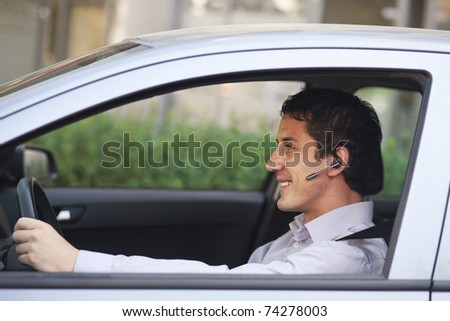 Smiling businessman driving a car with blue-tooth hands-free
