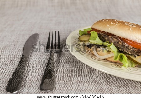 Fresh hamburger with a chop of marbled beef and fresh vegetables on a plate with a fork and knife.