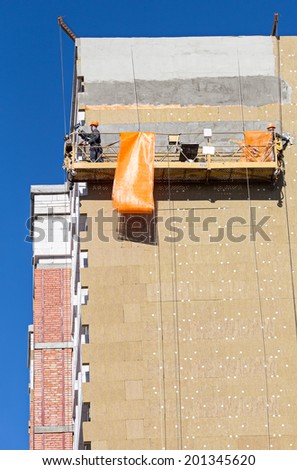 Construction workers plastering facade of high-rise building