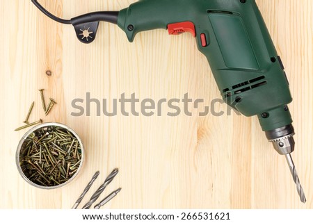 Electric drill with screws on wooden background