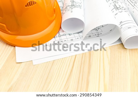 architectural blueprints with rolls of plans and safety helmet on wooden background
