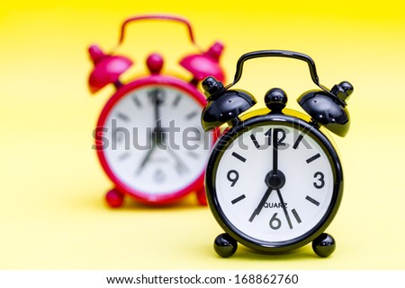 Two retro alarm clocks on yellow background displaying seven o'clock.