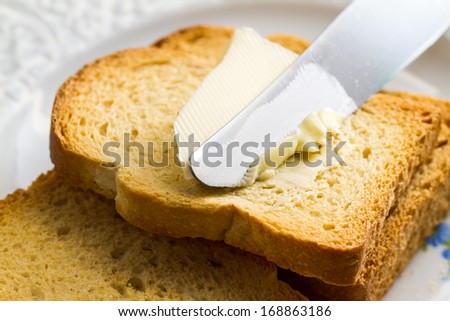 Spreading butter with a knife on sliced brown bread.