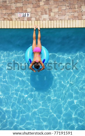 Looking down on a girl suntanning in a swimming poo on a pool float / pool ring, room for your text