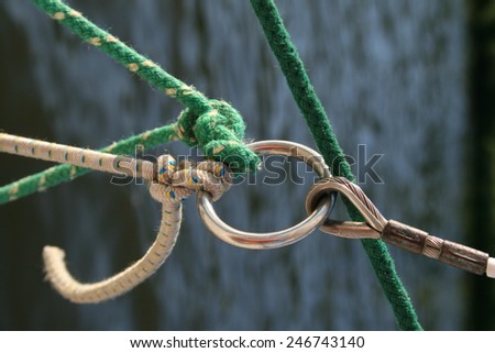Green and white rope tied to a metal o-ring as found in a sailing boat rig as part of the mast and sail rigging, which can be read as a visual metaphor for teamwork or friendship