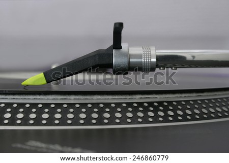 Close-up side-view of a deejay turntable\'s pick-up system, a Concorde style Ortofon Night Club needle with yellow tip placed on the rim of the record, speed markings in the foreground,