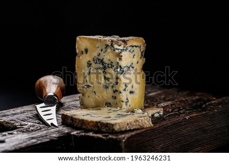 Semi-soft cheese with mold made from cows milk. The king of blue cheeses is Stilton. Piece of cheese on a dark wooden board and knife for cutting cheese. Low key image. Copy space