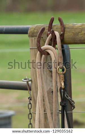 Ropes and chains hanging on a fence at a horse farm with horse shoes being used as hooks holding the ropes.