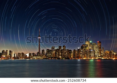 The skyline of Toronto lights up at night as the star rotate around the structures. This is a composite image of stars to the North. buildings are not in focus